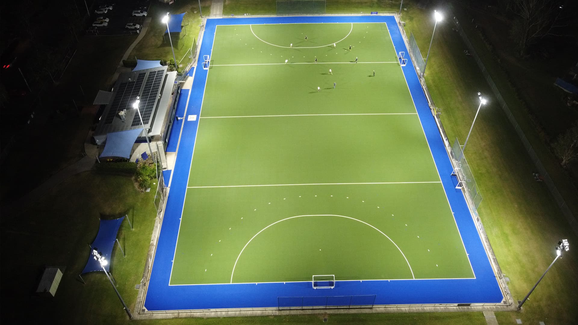 An aerial view of Ballinger Hockey Field at night with players gathered at one end of the field.