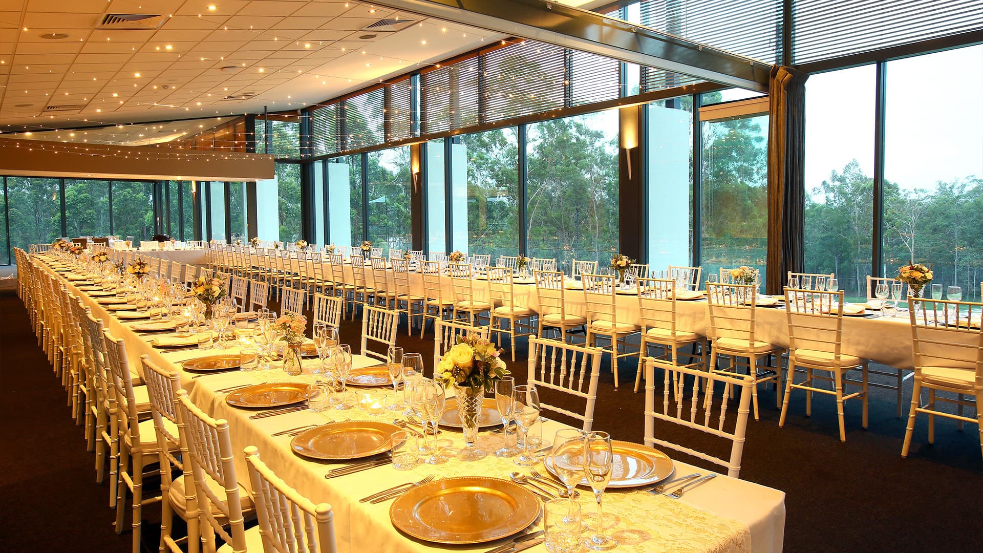 A wide angle view of two long tables set for dinner at the dining area at Brookwater Golf and Country Club.