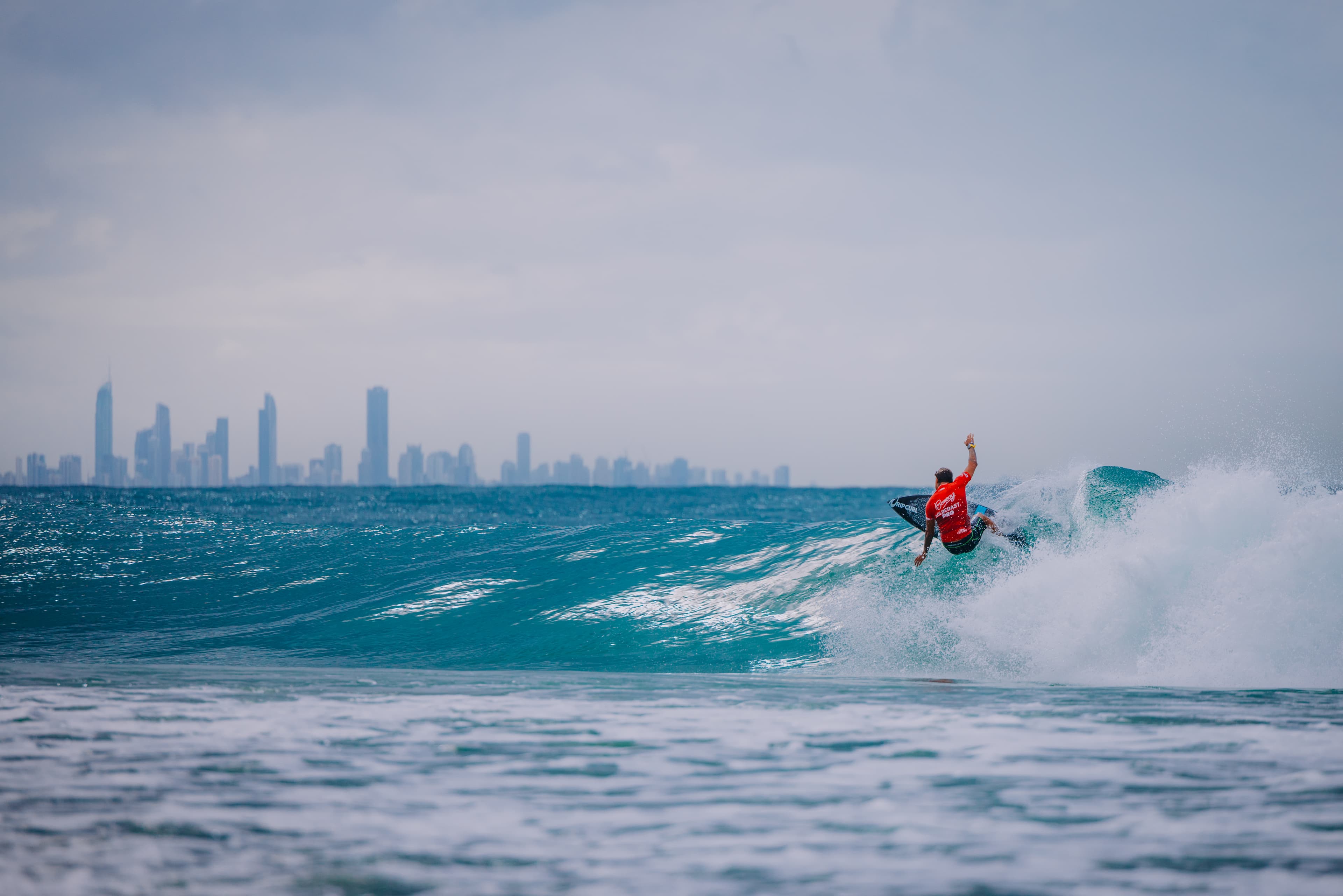 Surfer riding a wave at Coolangatta Beach with the high rises of Gold Coast's skyline in the background