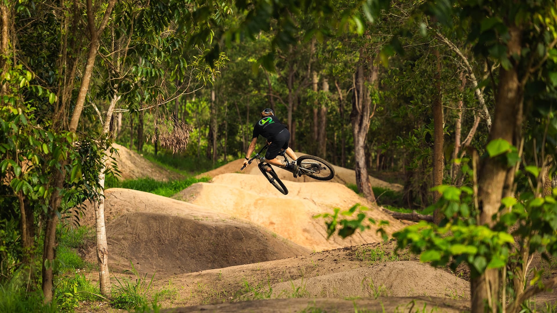 A mountain biker performing a jump on the dirt track at Finch Hatton MTB.