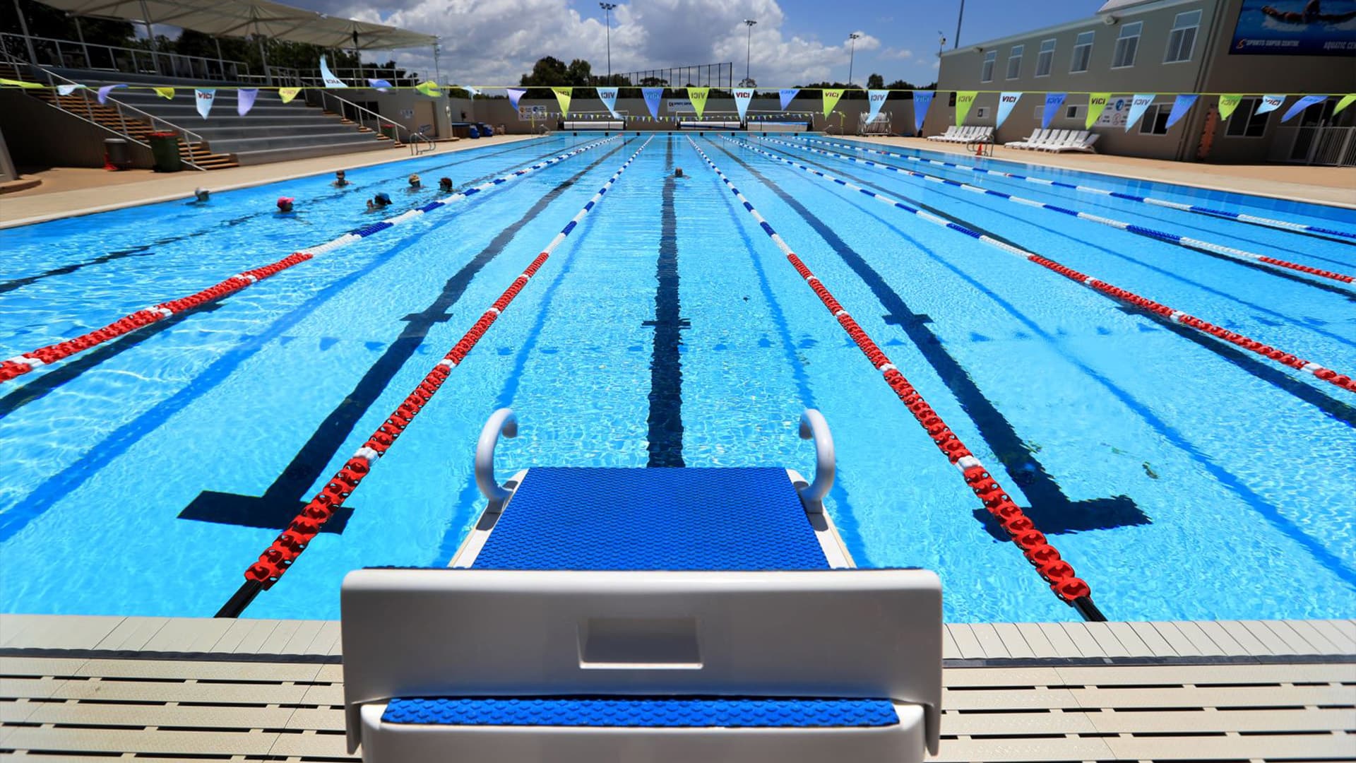 A wide angle close up view of a starting block at the swimming pool at the Gold Coast Performance Centre with swimmers gathered at one side of the pool.