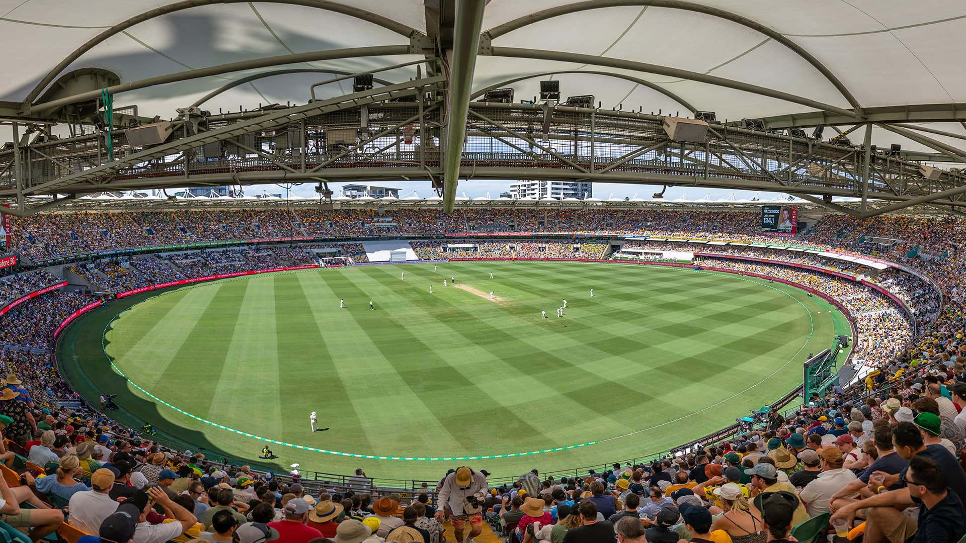 Internal high view of a full Gabba stadium during a game of cricket.