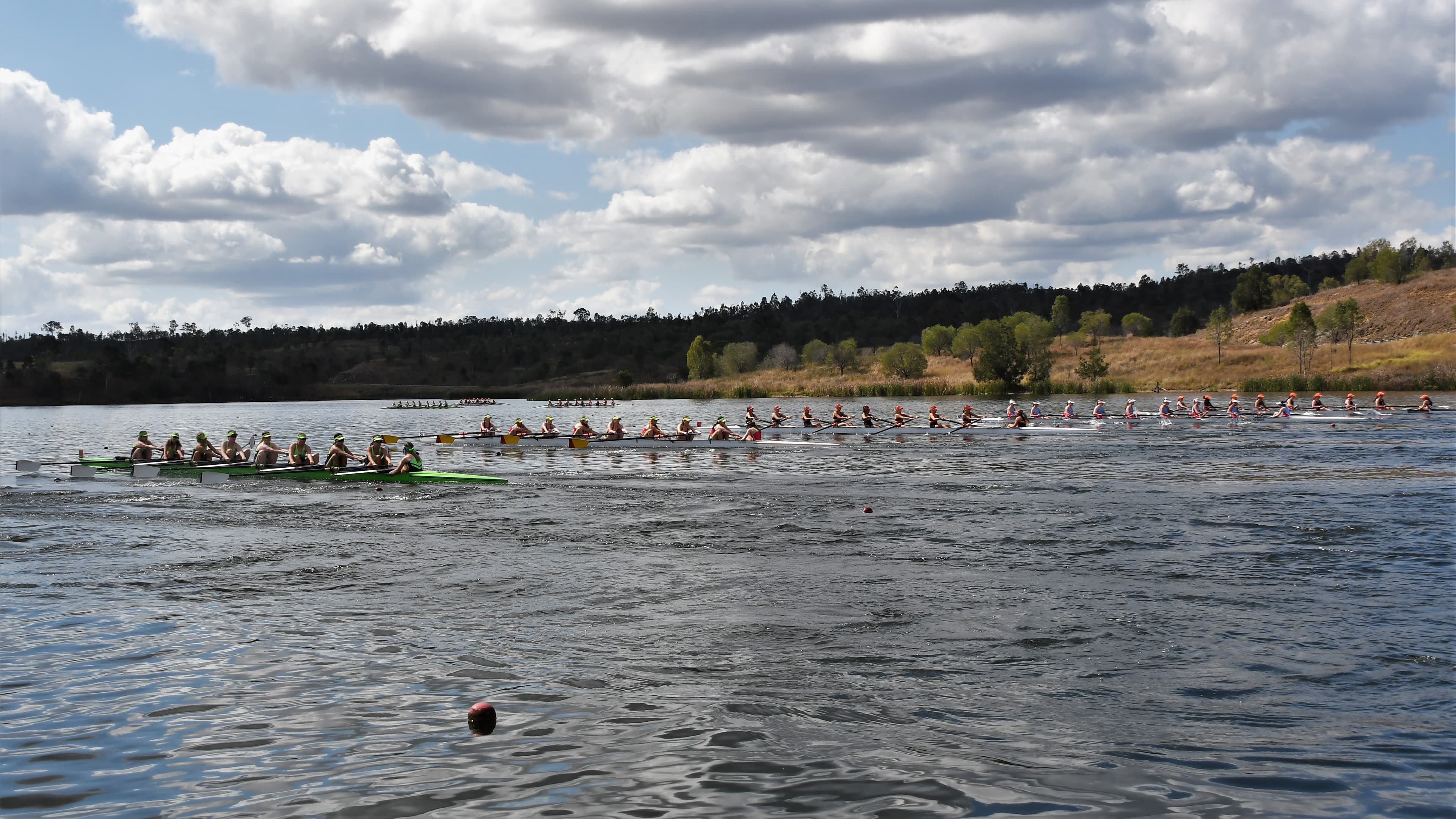 Wide shot of several 8-person rowing boats on the water at the Queensland State Rowing Centre