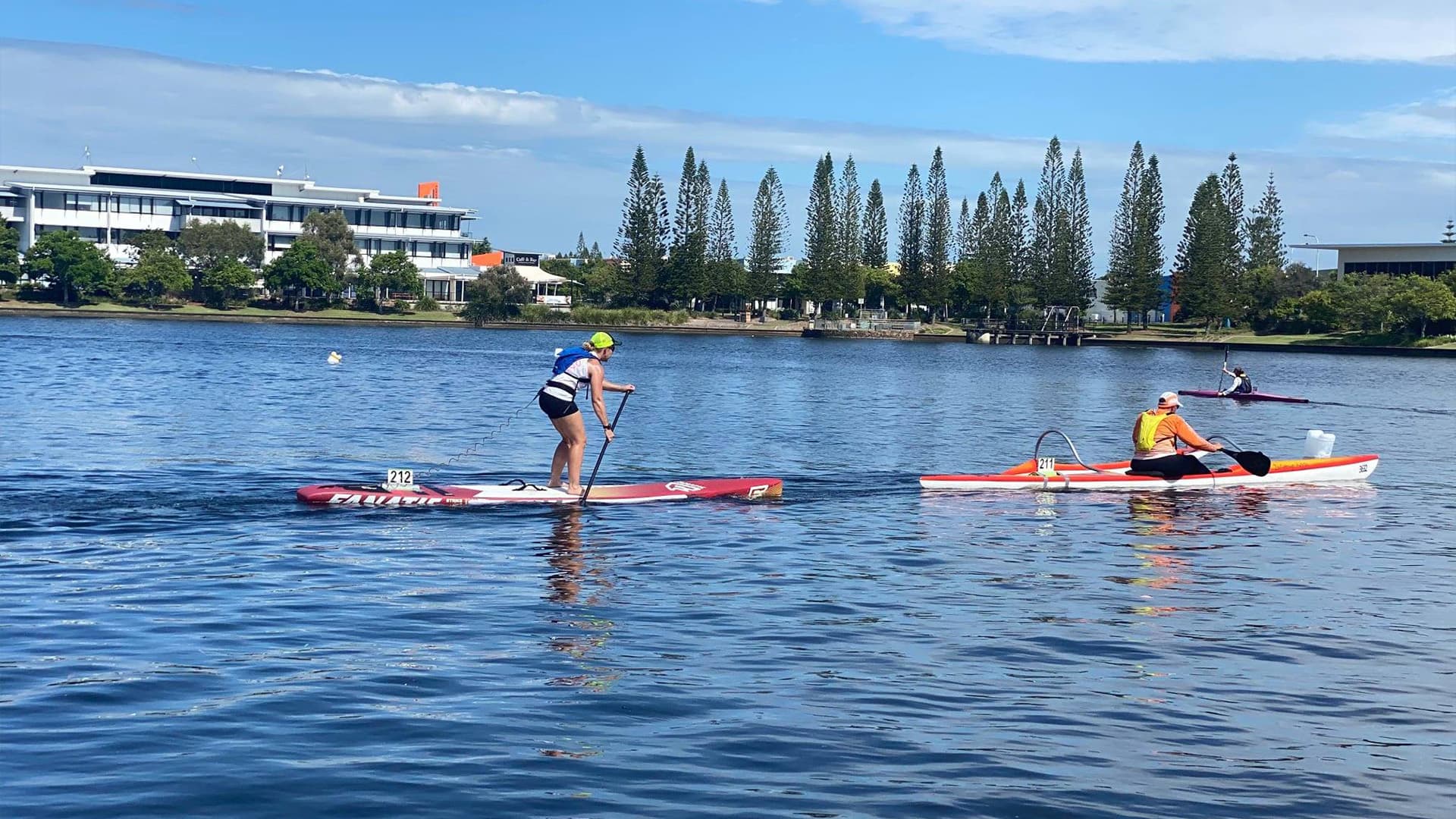 Three people on the lake paddle boarding and canoeing on a bright day.