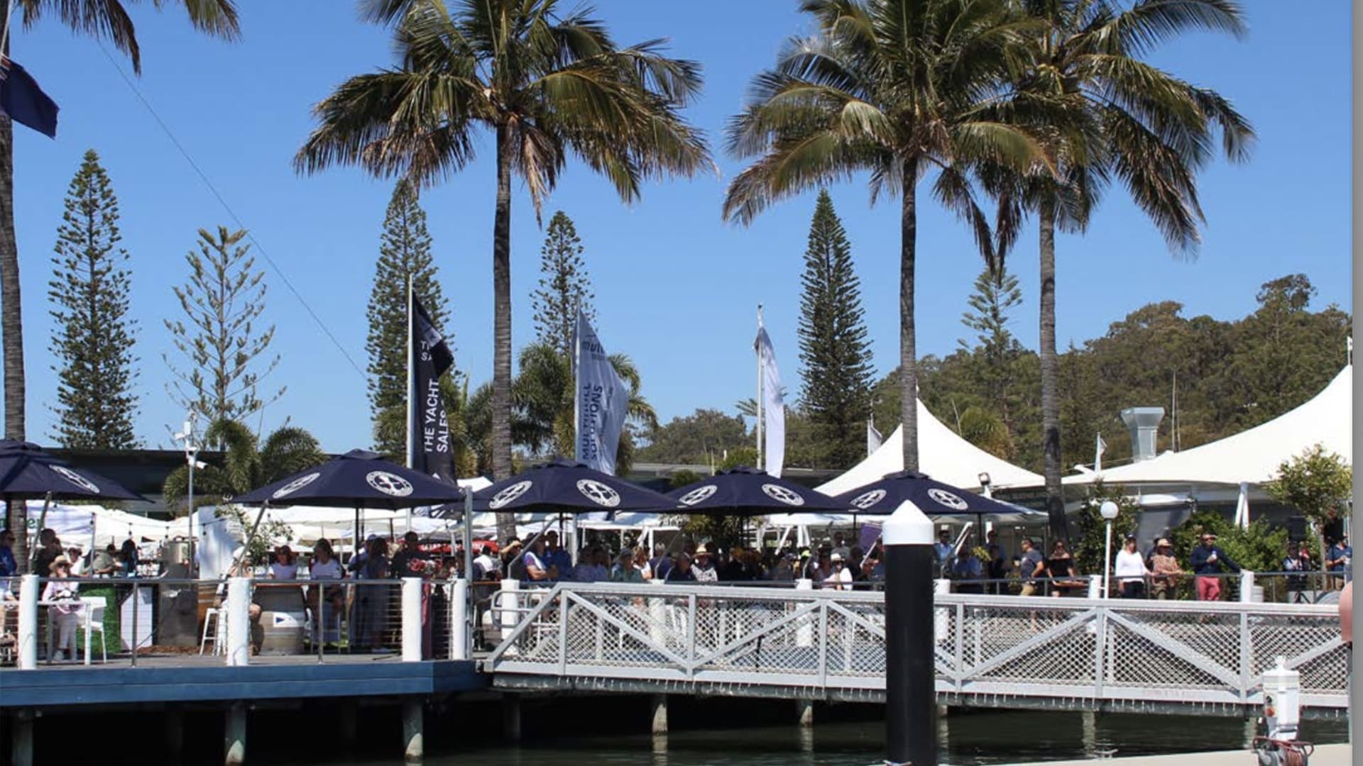 Groups of people sitting under restaurant umbrellas at the Royal Queensland Yacht Squadron.