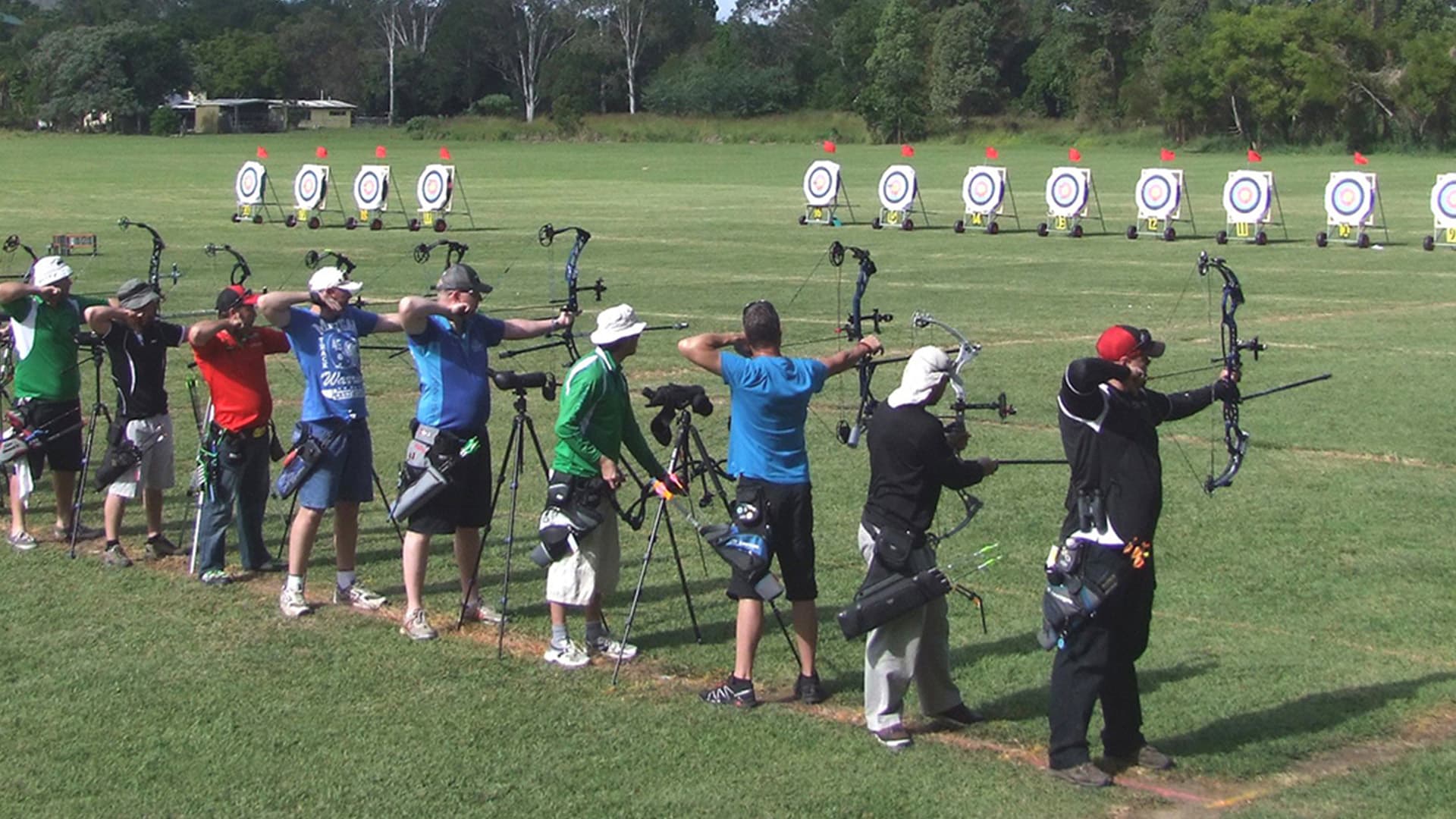 9 people standing in a line, preparing to shoot towards a line of targets about 20 meters in front of them.