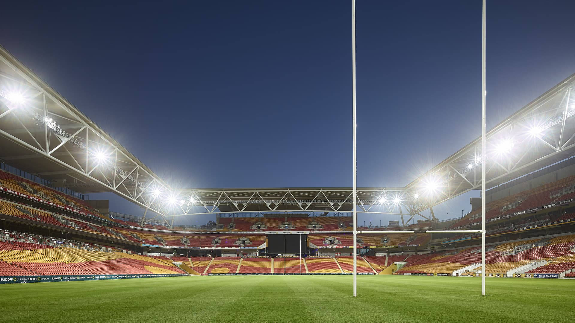 Photo from behind the goal at Suncorp Stadium in the evening with overhead lights on, empty stands and no players on the field.