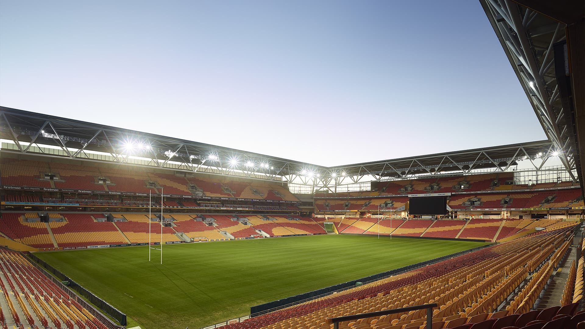 Suncorp Stadium at sunset with overhead lights on, empty stands and no players on the field.